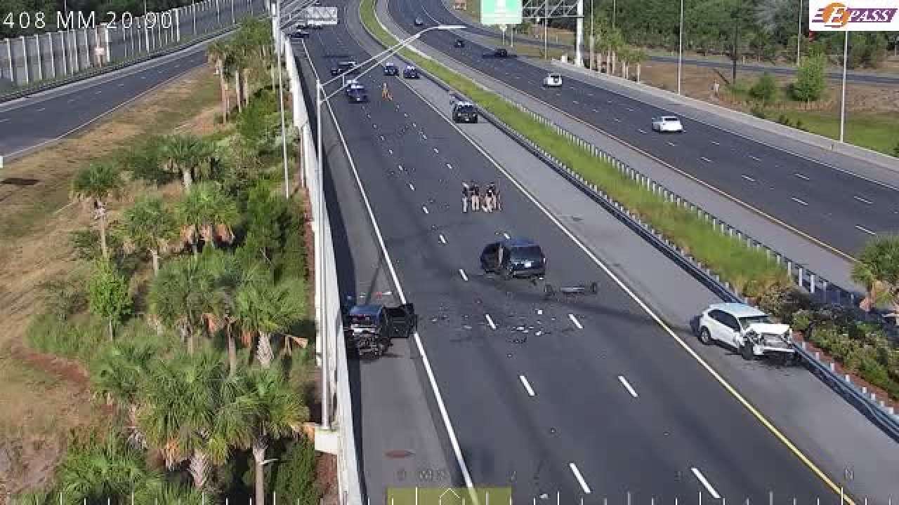 A traffic camera image shows a crash on SR-408 eastbound at mile marker 20.9, with two damaged vehicles blocking the right lane. Several responders are on the scene, and traffic is moving slowly in the remaining lanes. The image includes an E-PASS logo and palm trees along the highway.