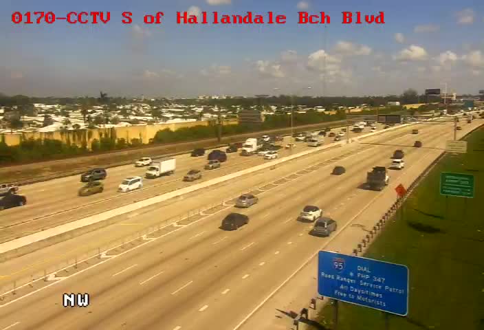 CCTV camera capturing a highway south of Hallandale Beach Boulevard, with northbound and westbound lanes showing light to moderate traffic under clear but potentially smoky conditions, including a road sign for Dial-A-Ride and Florida Highway Patrol.
