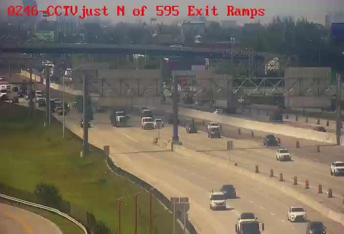 CCTV footage of a multi-lane highway just north of the 595 exit ramps in South Florida, showing moderate traffic with vehicles including cars and trucks moving southbound under hazy skies likely due to wildfire smoke.