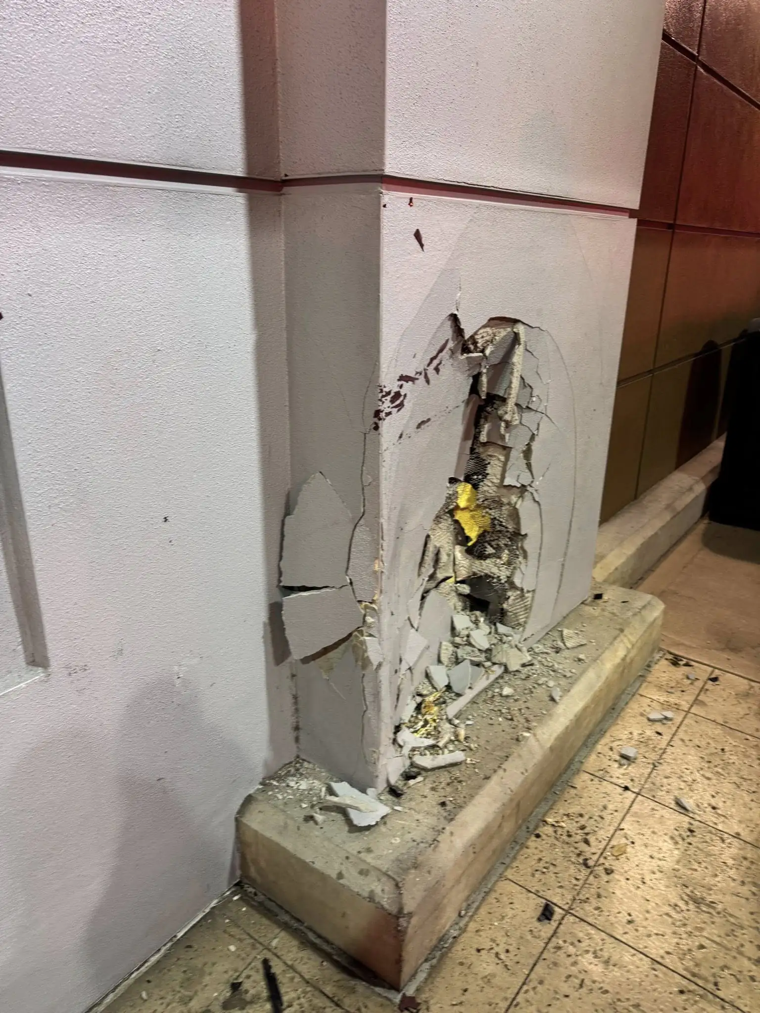 A close-up image shows extensive damage to the building's wall, with large chunks of concrete and plaster broken away, revealing underlying insulation and wiring, and scattering rubble across the tiled floor. Credit: Sebring Fire Department.